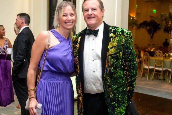 Smiling woman in purple dress with man in sequined blazer at Believe Ball event.