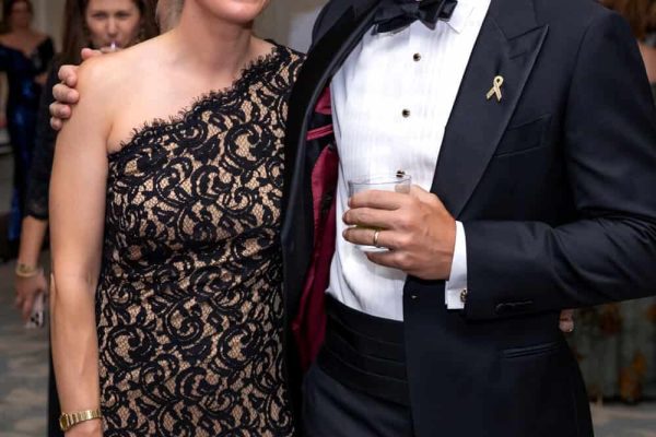 Elegant couple at Believe Ball event in formal attire with a gold ribbon pin.