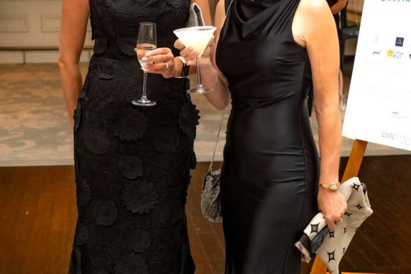Two women in elegant black evening gowns at Believe Ball event.