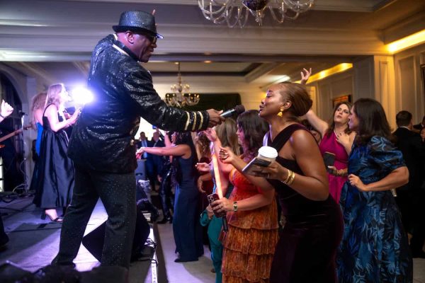 Performer in glittery jacket and hat interacts with audience at Believe Ball event.
