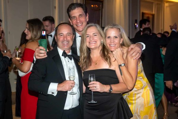 Group of four smiling people at a formal event, holding drinks, celebrating together.