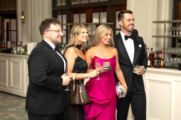 Elegant group of four at a formal event with drinks and smiles.