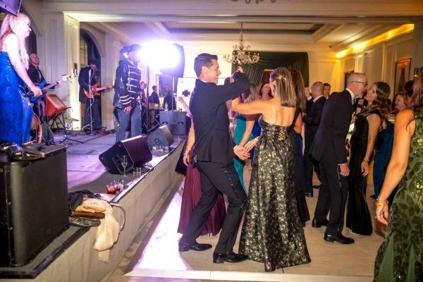 People dancing at a formal event with live band on stage in elegant ballroom.