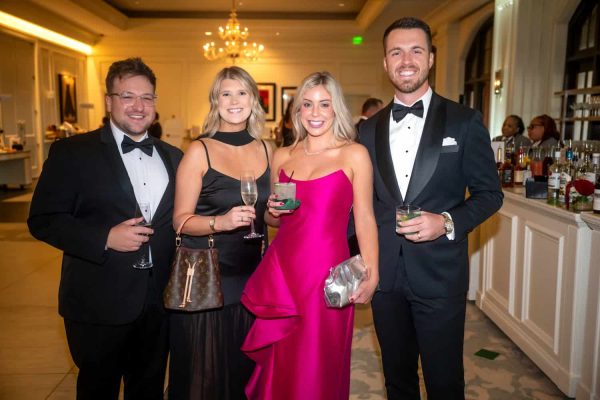 Elegant group of four at Believe Ball in formal attire, smiling and holding drinks.