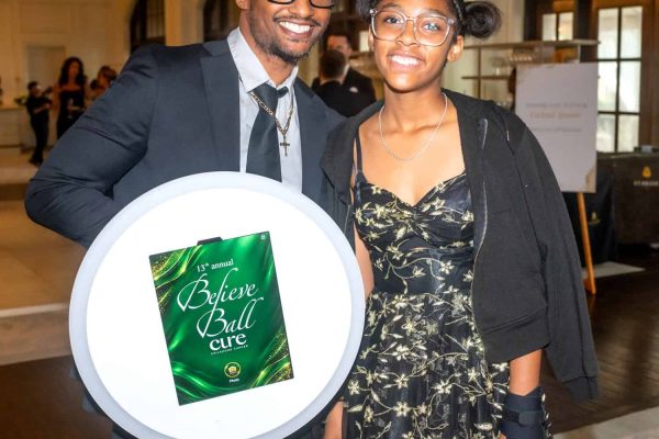 Two smiling individuals at Believe Ball event holding a sign for Cure.