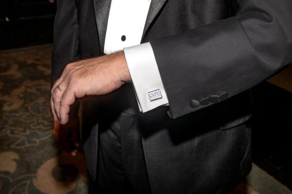 Close-up of a man in a tuxedo with a Cure cufflink on the sleeve.