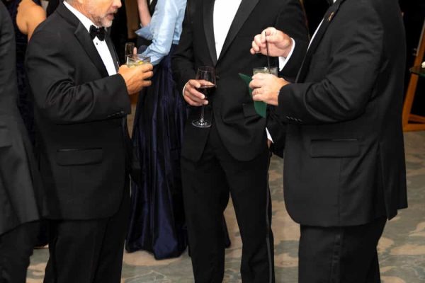 Elegant men in tuxedos enjoying drinks at Believe Ball event.