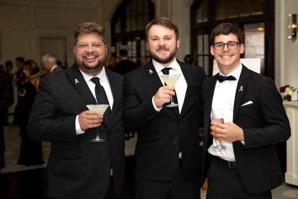 Three men in tuxedos at Believe Ball event holding cocktails and smiling.