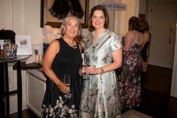 Two women at Believe Ball event holding wine glasses, smiling for the camera.