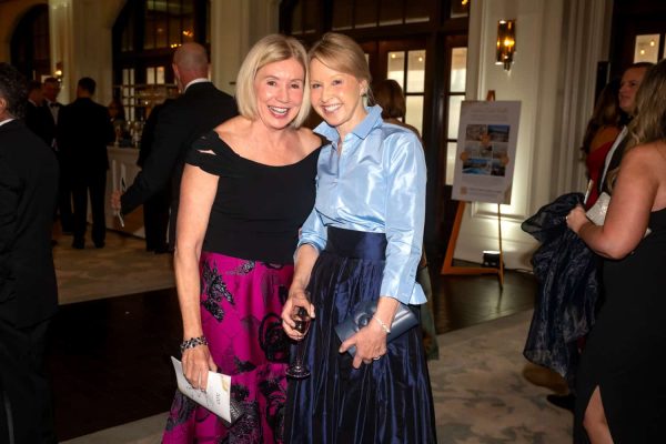 Two women smiling at the Believe Ball event, dressed elegantly in a grand venue.