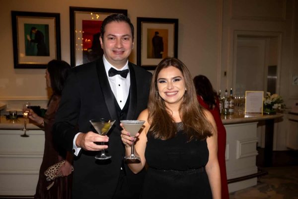 Elegant couple at Believe Ball holding cocktails in formal attire.