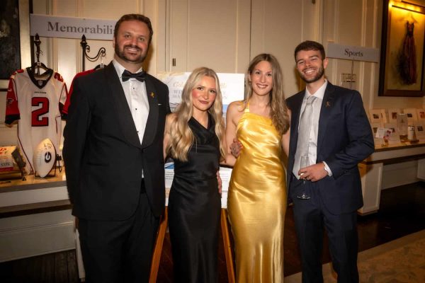 Group of four elegantly dressed people at Believe Ball event in a decorated venue.